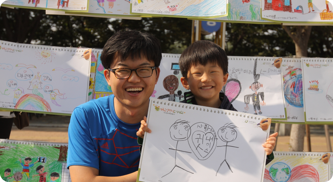 굿네이버스 가족그림편지쓰기대회에 참여하여 스케치북을 들고 환하게 웃는 아빠와 아들의 모습