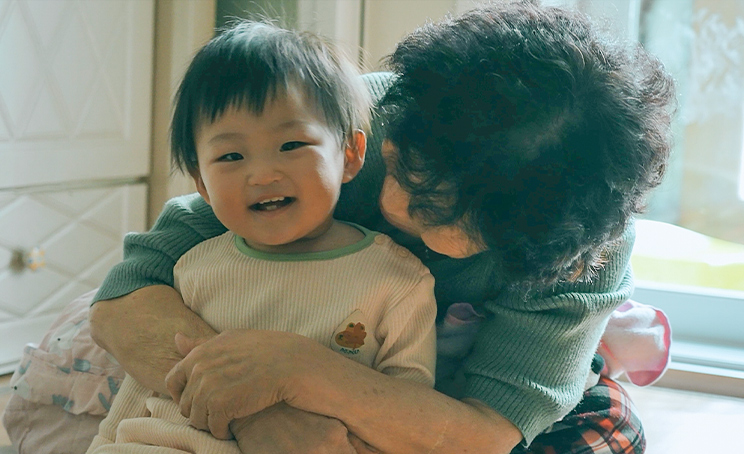 재희가 할머니 품에 안겨서 환하게 웃고 있다.
