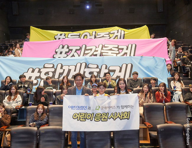 #들어줄게 #지켜줄게 #함께할게 및 어린 의뢰인과 굿네이버스가 함께하는 어린이 응원 시사회 현수막을 들고 있는 감독, 배우, 관객