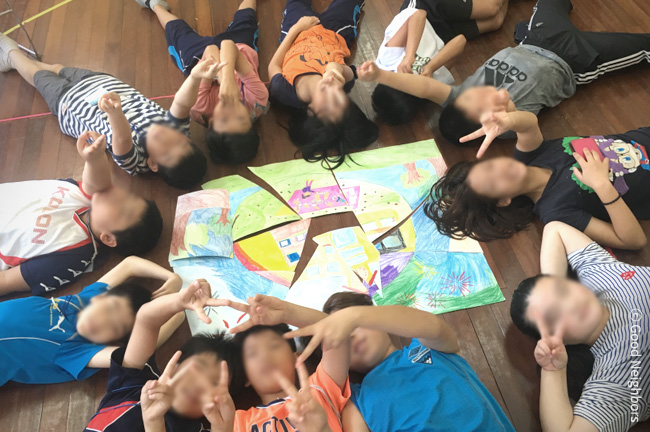 함께 누워 브이를 그리고 있는 희망나눔학교 참가 아동들 이미지