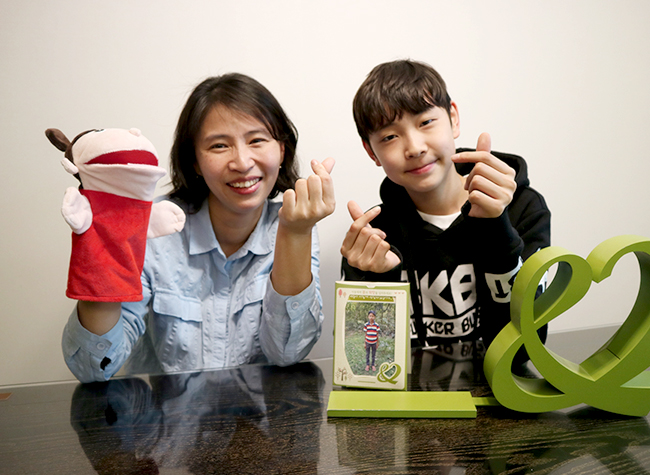 결연아동 프로필 앞에서 함께 하트 포즈를 하고 있는 변지혜 회원님과 아드님 이미지