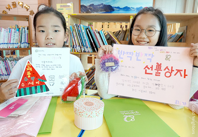 직접 제작한 홍보 판넬을 들고 환하게 웃고 있는 휘은, 가은 자매 이미지