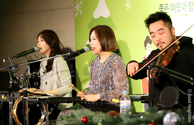 좋은 이웃 콘서트에서 노래를 부르며 악기를 연주하는 옥상달빛과 바이올린 연주자 이미지