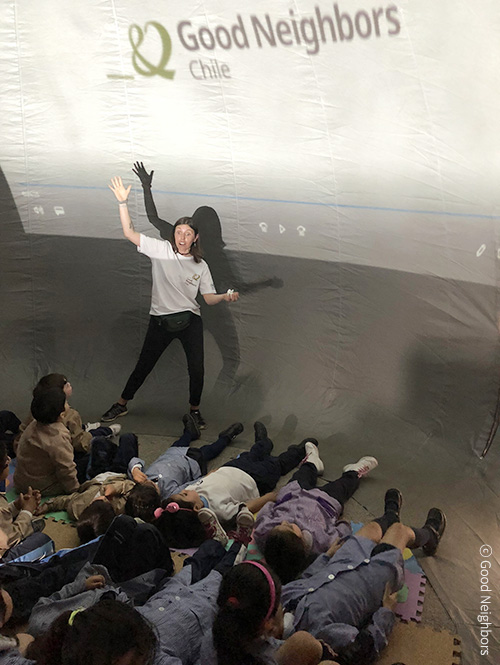 이동식 돔교육장 안에서 여자 교사 1명이 나와 천장에 빔을 쏘며 교육을 진행하고 아이들은 바닥에 누워 교육을 듣고 있는 이미지