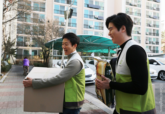 왼쪽 최수종씨는 박스를 들고 오른쪽 이장우씨는 쌀을 들고 웃으며 걷고 있는 이미지
