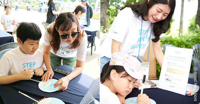 굿멤버스데이 부스에 참여한 좋은 이웃들에게 지구촌 아동들의 물 부족 현실을 설명하는 봉사자 이미지