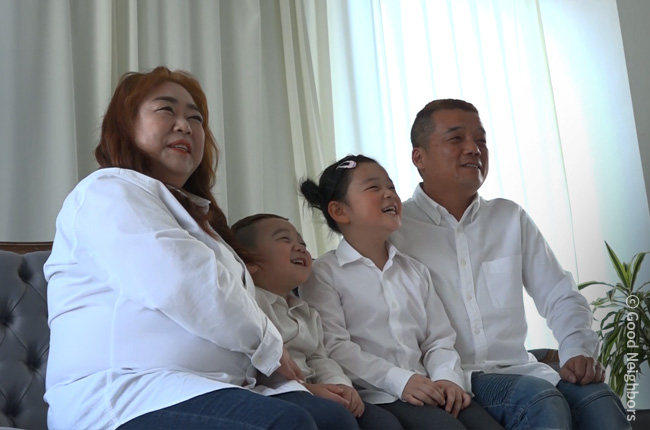 첫 가족 사진을 찍기 위해 흰 셔츠에 청바지를 입고 밝게 웃고 있는 성법이 가족