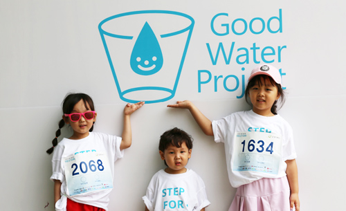 굿워터프로젝트 로고 앞에서 환하게 웃고 있는 STEP FOR WATER 참가 아동 이미지